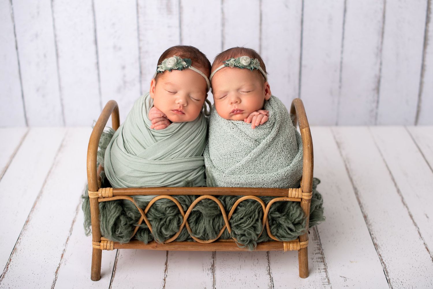 Two swaddled newborns resting together in decorative wooden bench.