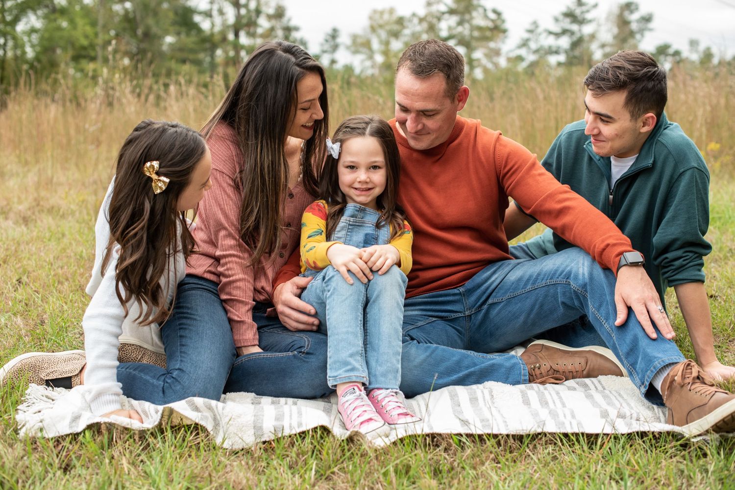 Happy family of four sitting together on blanket in tall grass field.