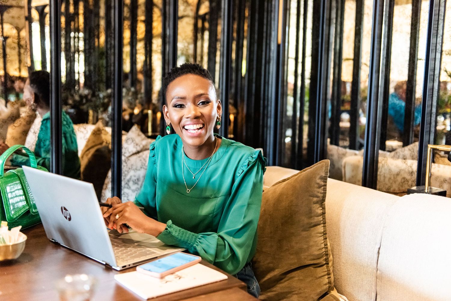 Cheerful pose in green sweater while working on laptop in modern cafe setting.