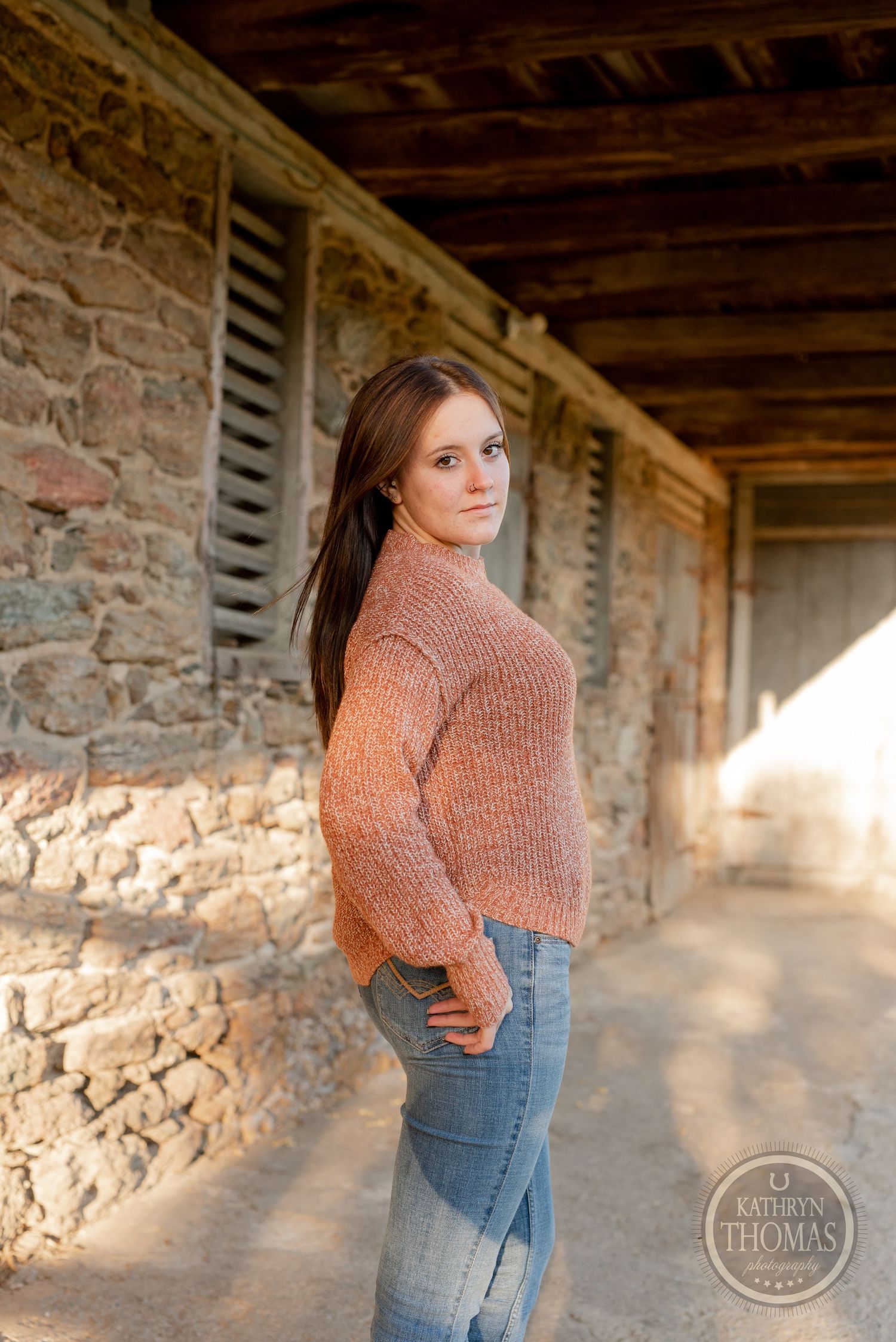 Person in peach sweater poses against historic stone building with wooden beams.