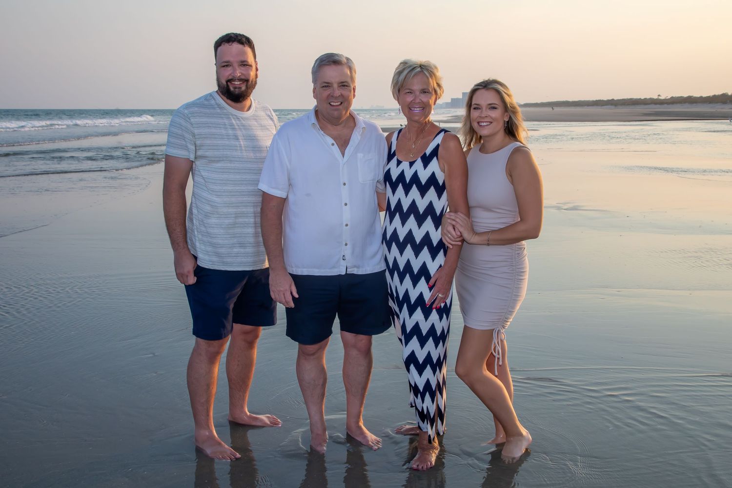 Small group standing together on beach at dusk with ocean waves behind them.