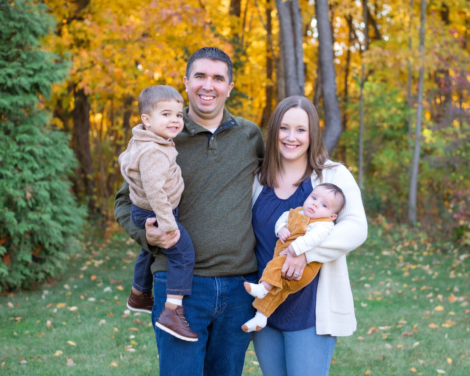 A family of four poses for a portrait in front of colorful autumn trees.