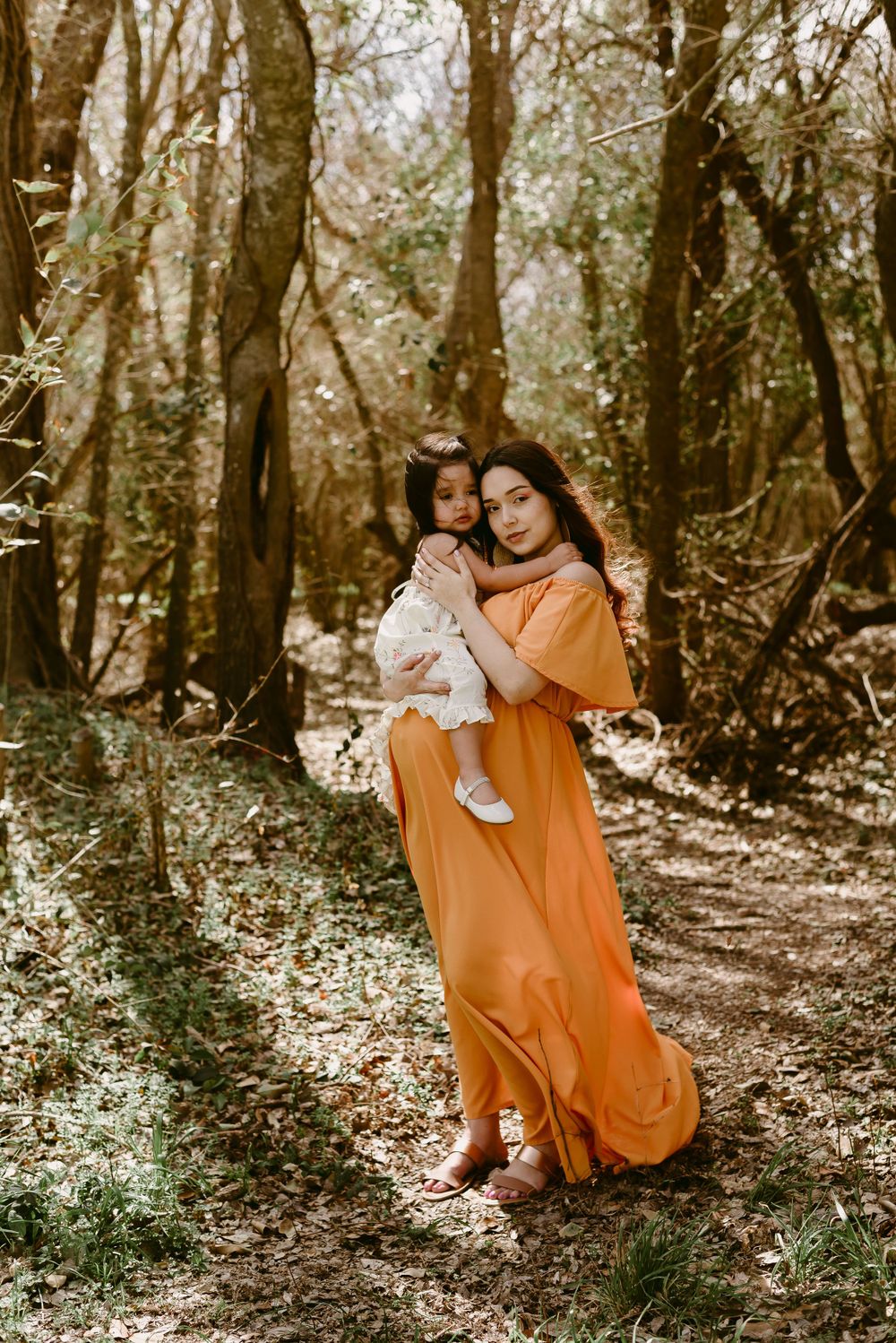 A tender outdoor portrait in a forest setting featuring flowing orange dress and intimate family moment.