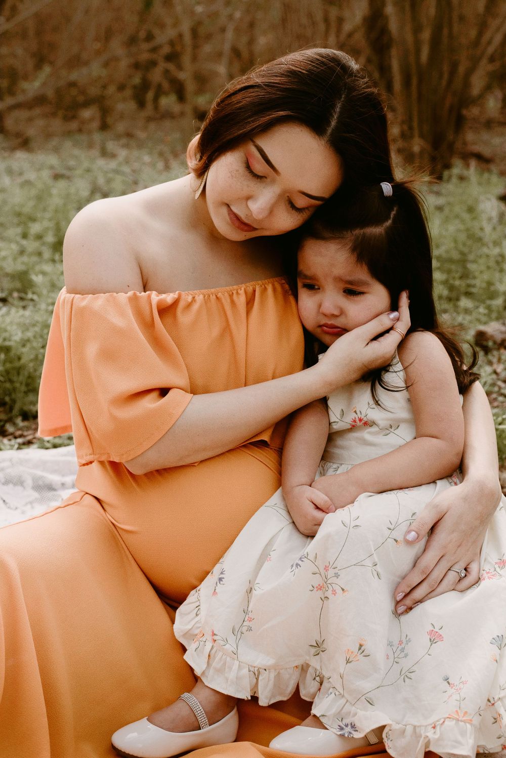 Tender moment between parent and child sitting together in matching orange and white dresses.
