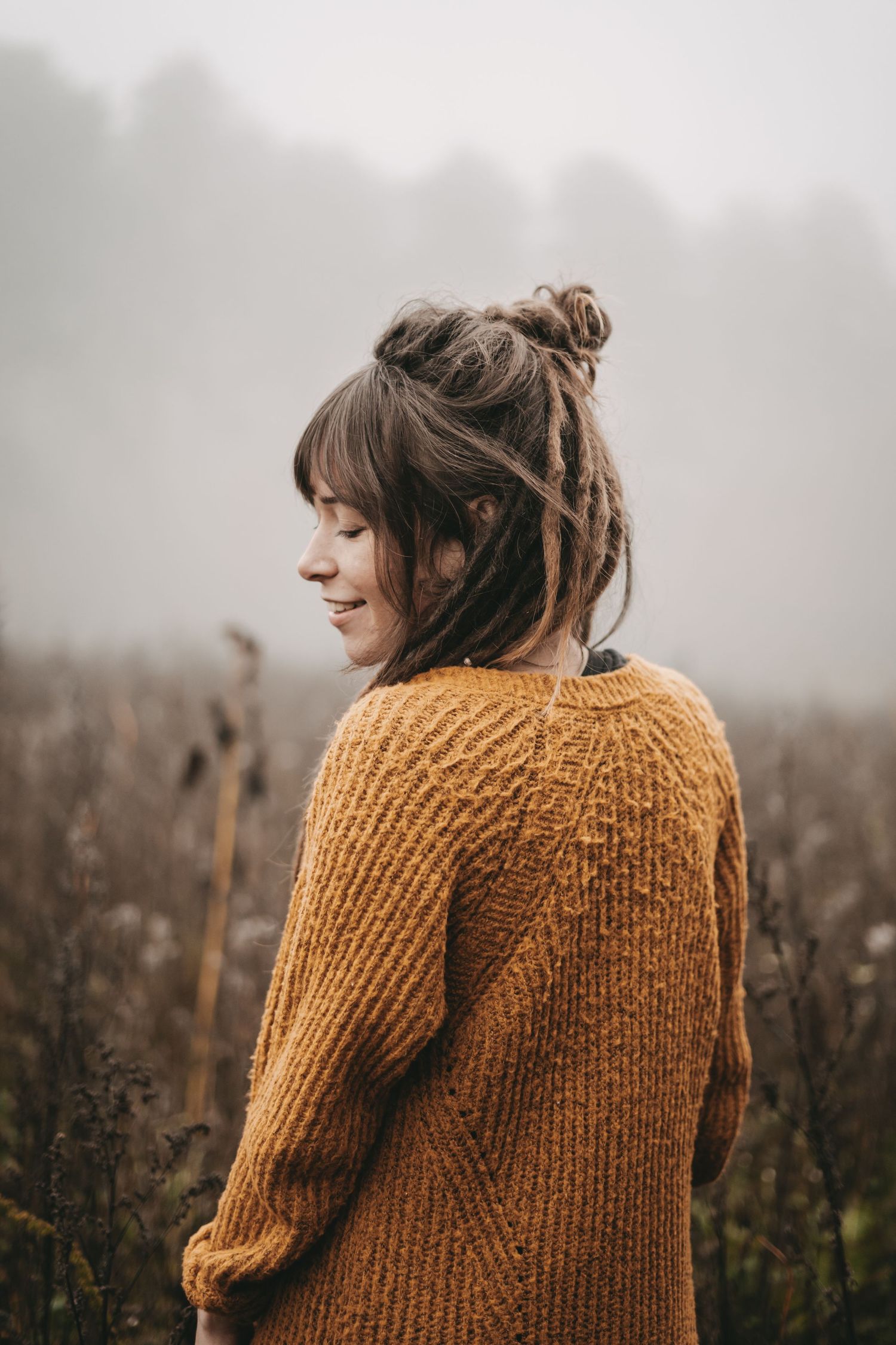 Person wearing mustard knit sweater photographed from behind in foggy setting.