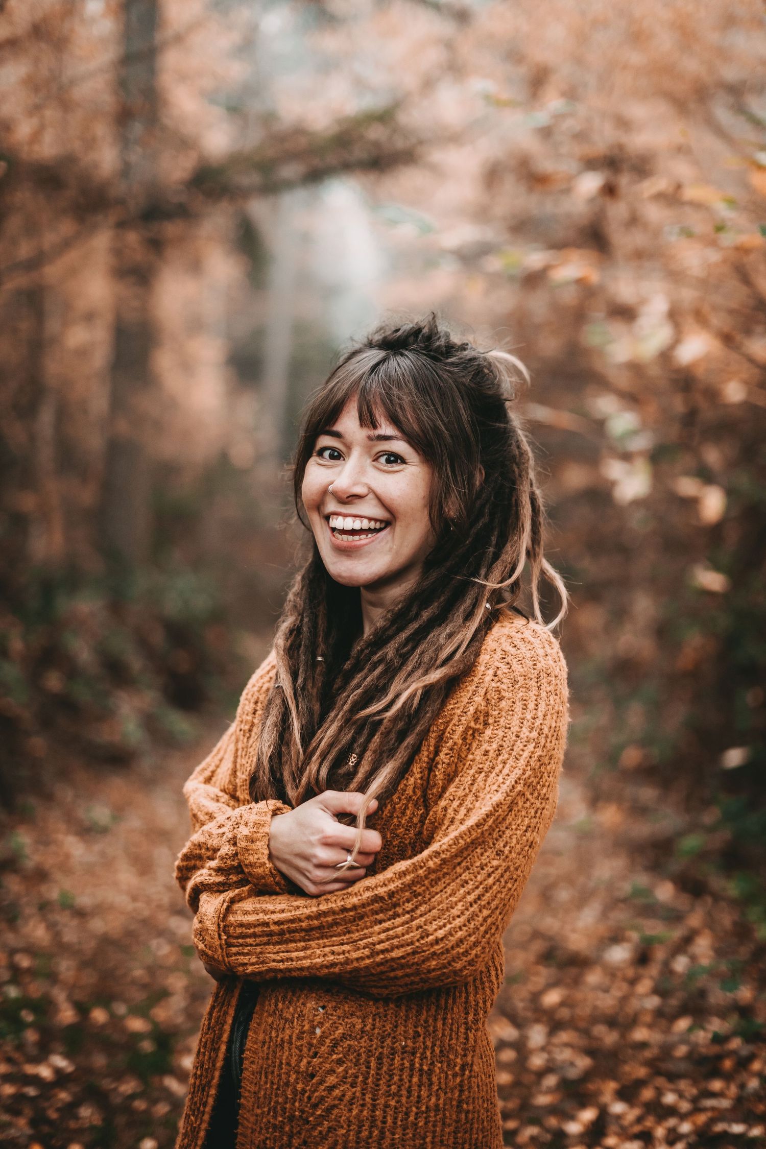 Person in chunky orange sweater laughing joyfully in autumn forest setting.