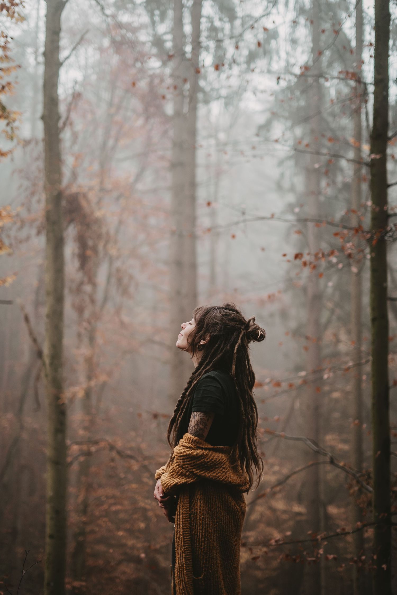 Figure in cozy knit sweater walking through misty autumn forest.