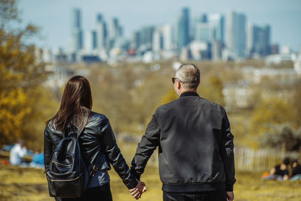 A couple holds hands while looking at a city skyline on an autumn day.