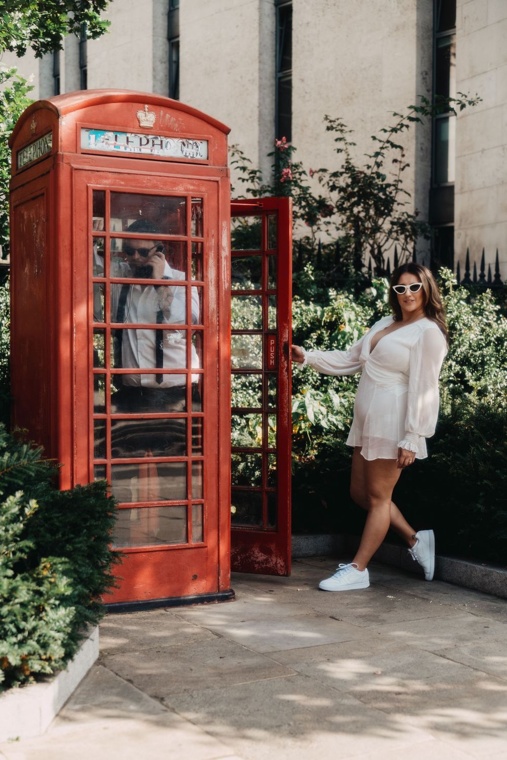 Fashion portrait by iconic red London phone booth with elegant white outfit.
