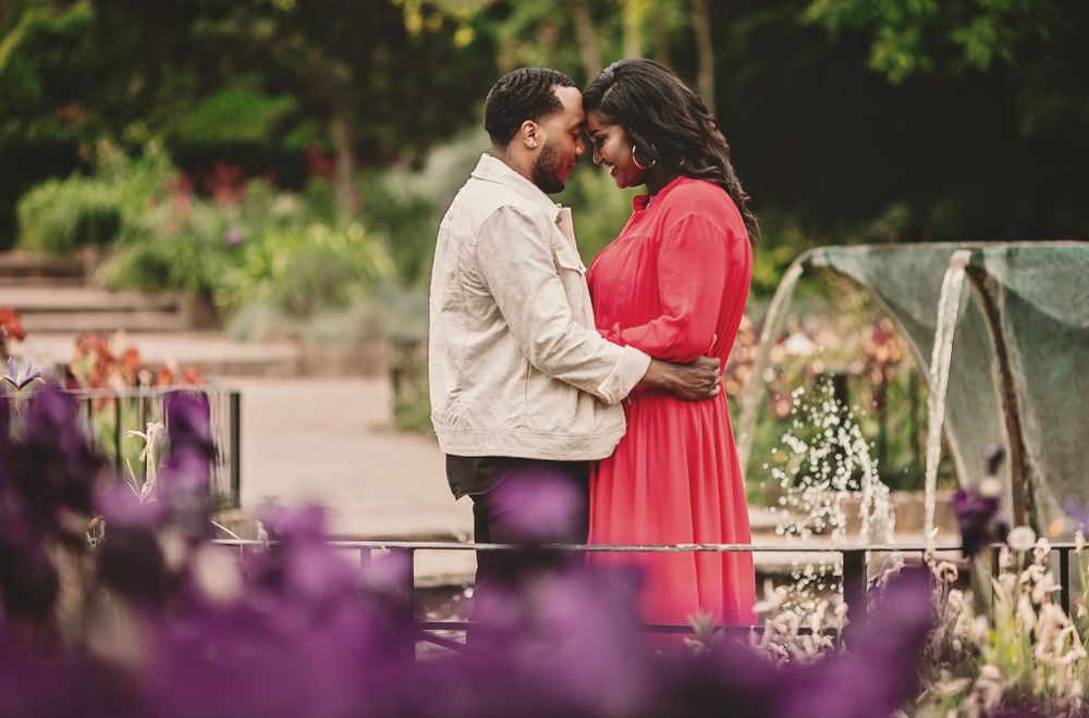 A couple shares a romantic moment on a bridge surrounded by purple flowers.