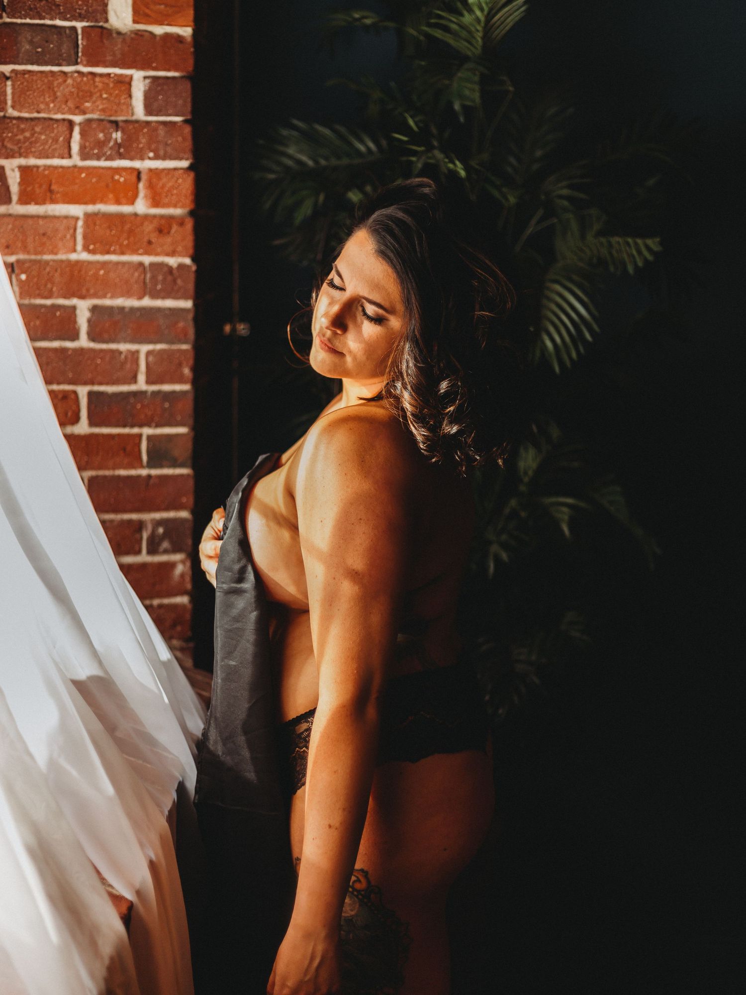 Dramatic portrait against brick wall and palm plants with flowing white fabric.