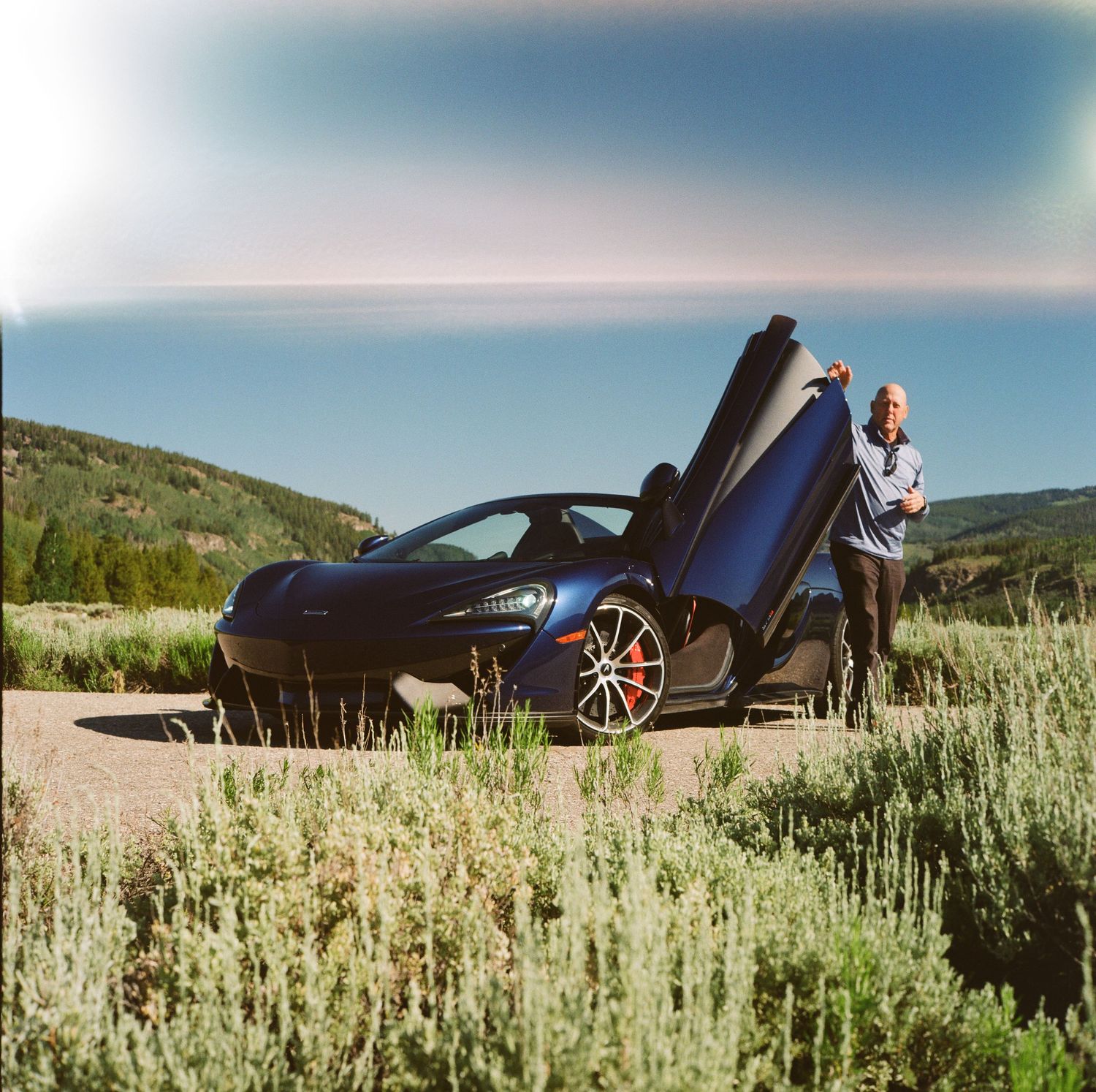 Blue BMW sports car parked in scenic mountain landscape with butterfly doors open.