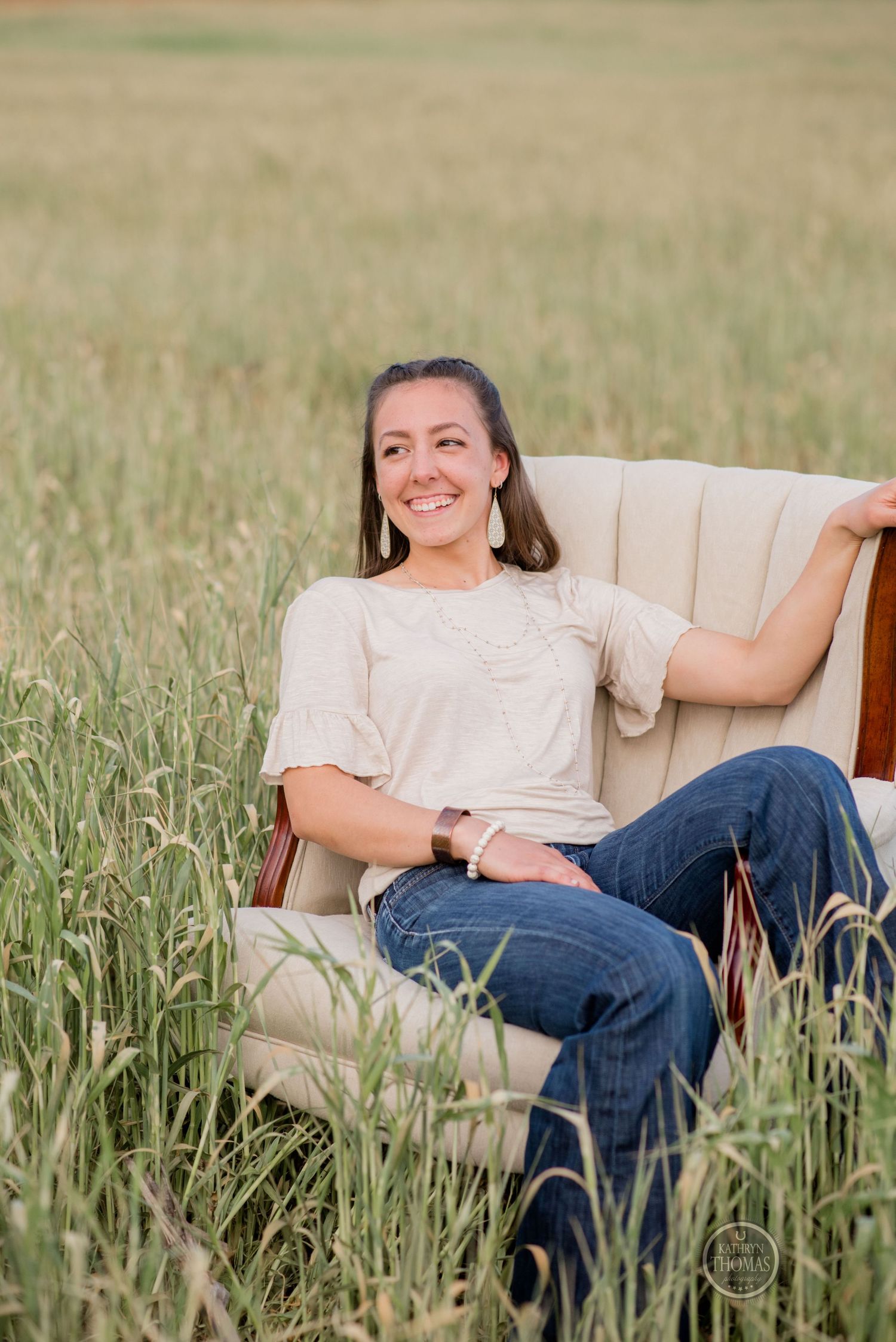Someone relaxes in a vintage beige armchair surrounded by tall grass in a field.