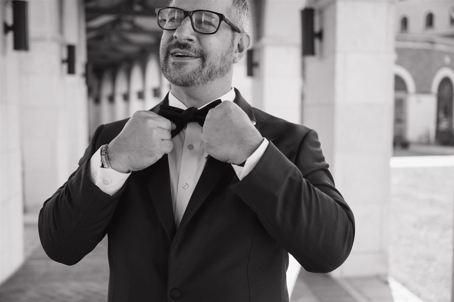 Formal portrait of person adjusting bowtie while wearing a classic black tuxedo.
