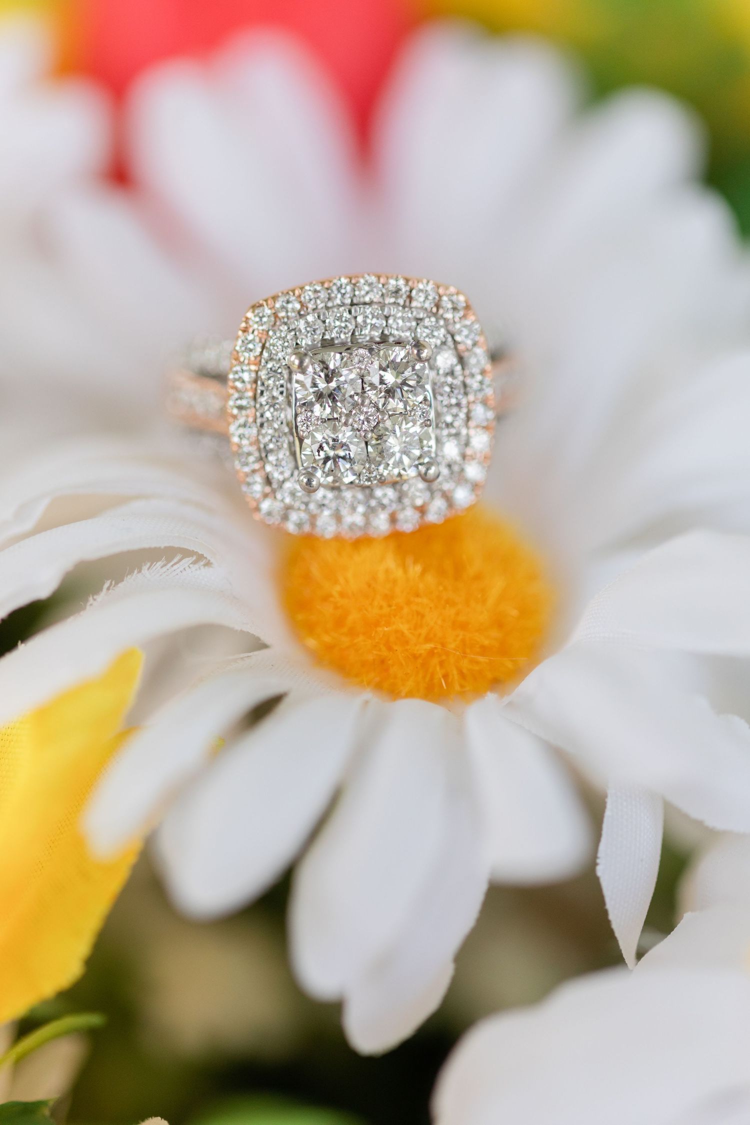 Sparkling diamond engagement ring displayed on a white daisy flower with yellow center.