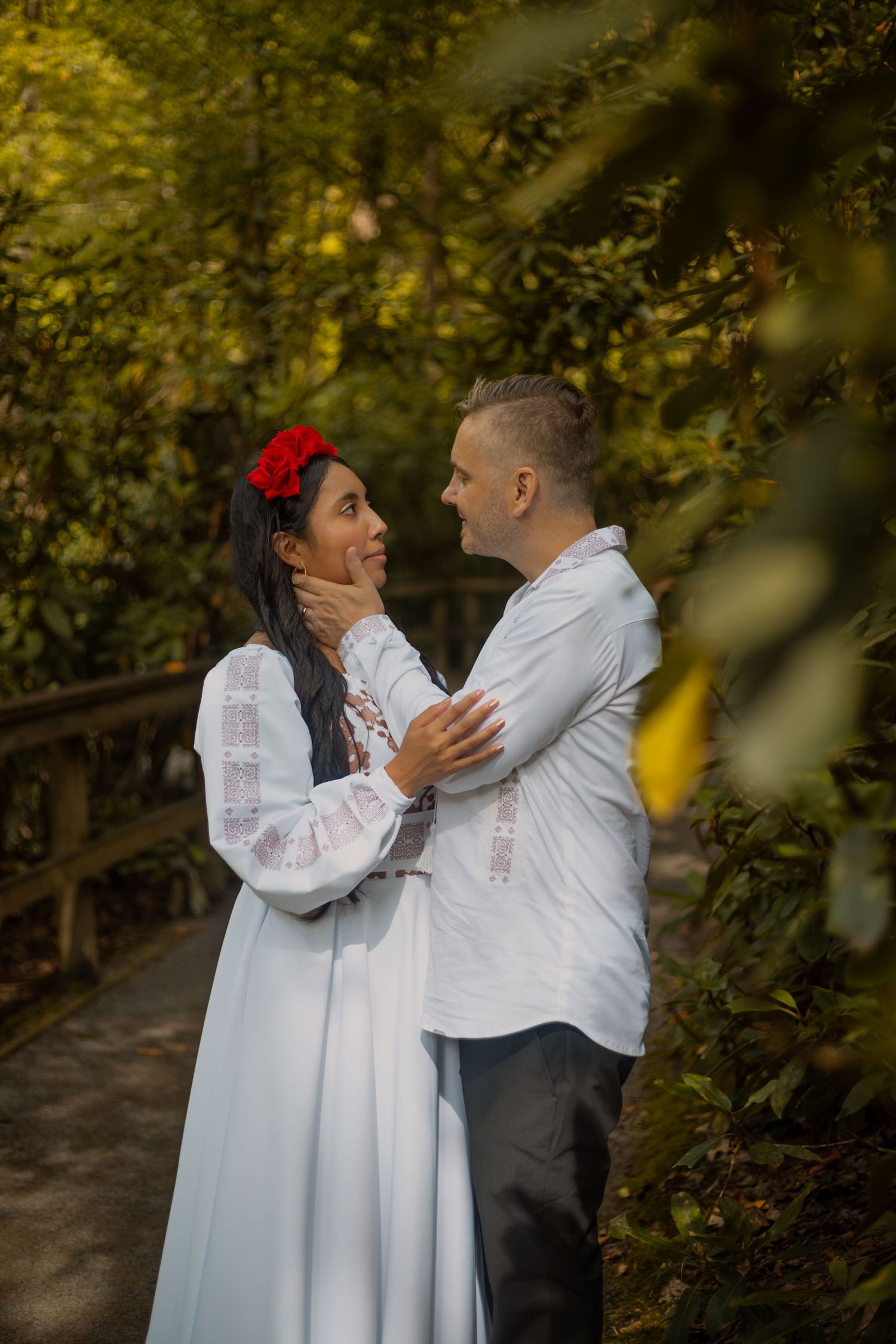 Couple in white traditional outfits embrace during outdoor photo session.