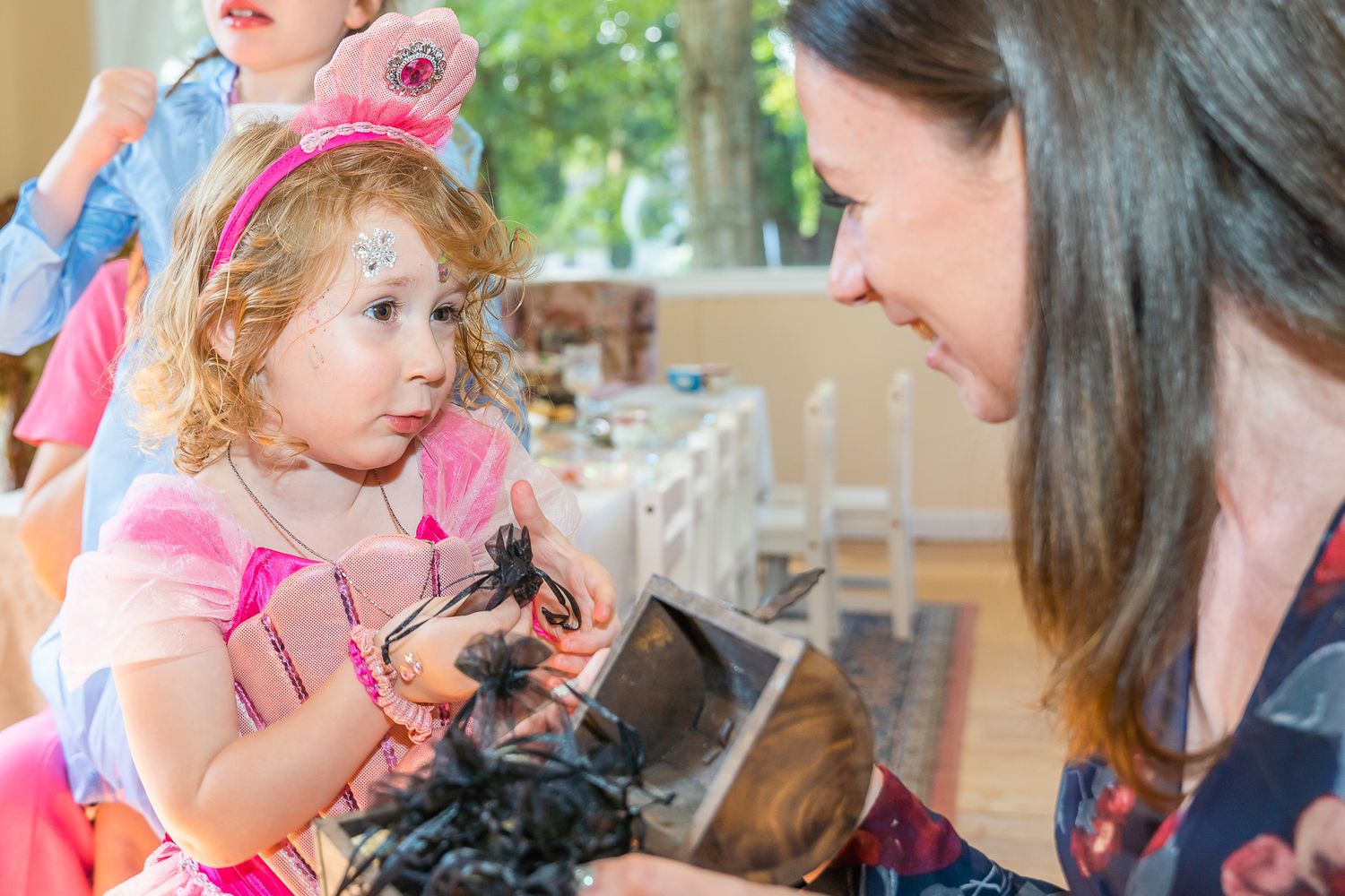 Young girl in pink costume holding a dark object while a woman looks on at a party.