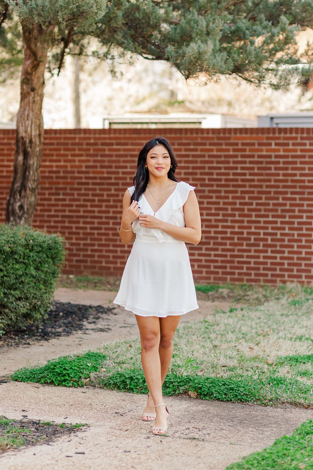 Woman in white summer dress walks barefoot along garden path near brick wall.
