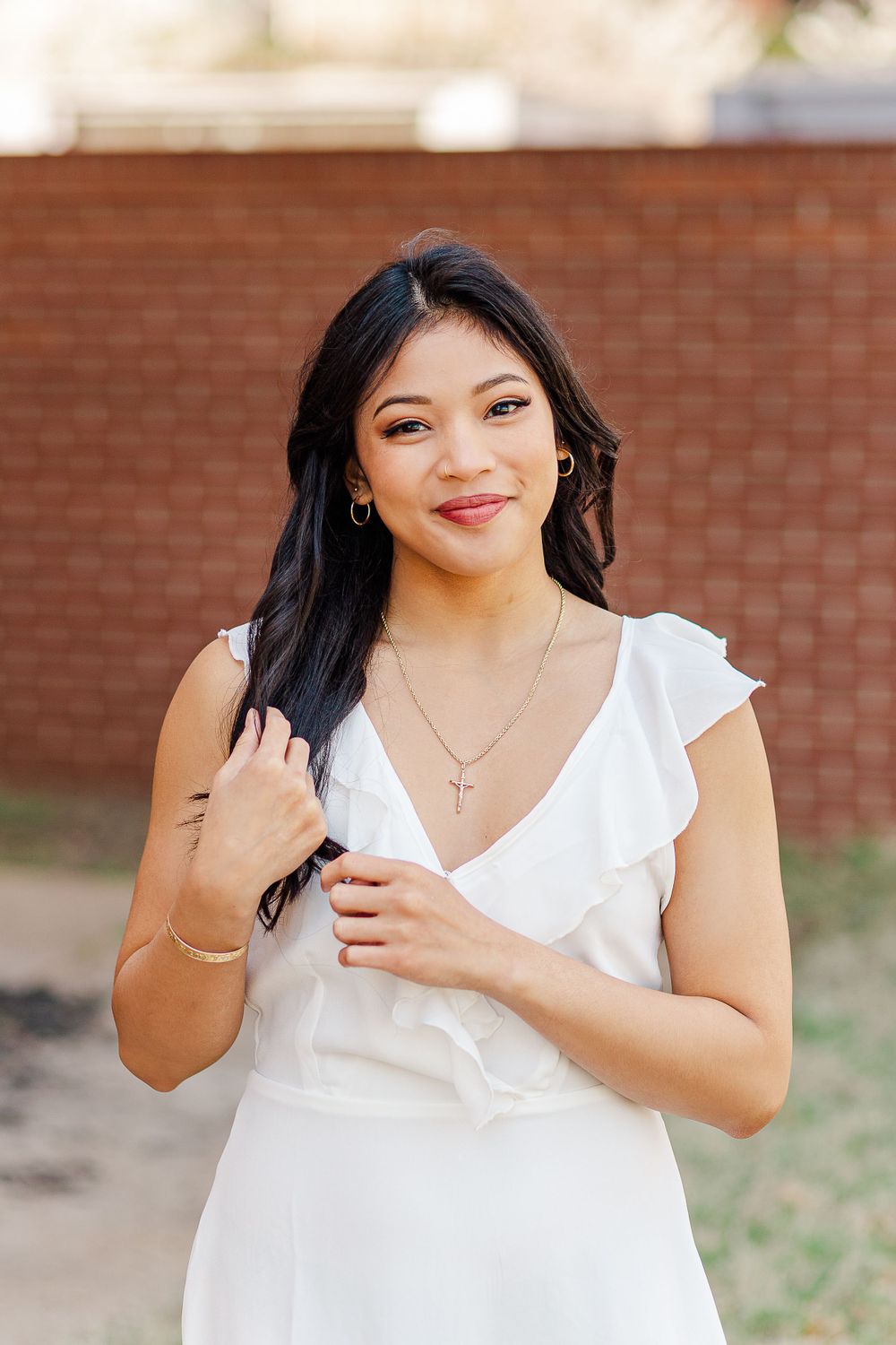 Close-up portrait of woman wearing white dress and delicate necklace against brick background.