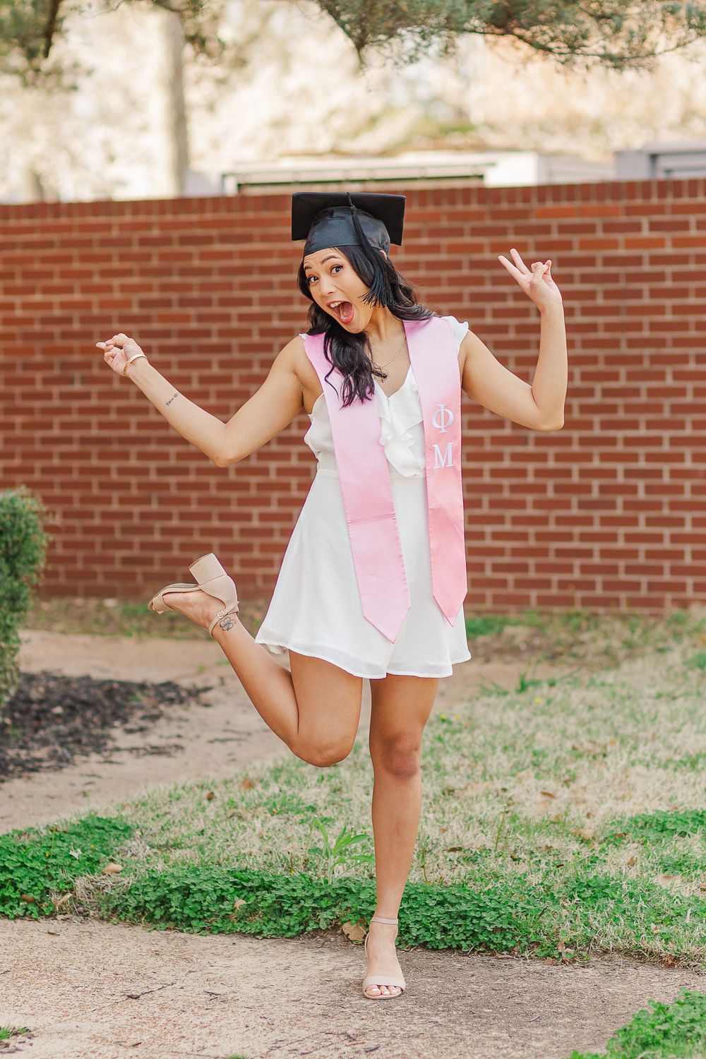 Excited graduate in cap and gown jumps playfully during photo session.
