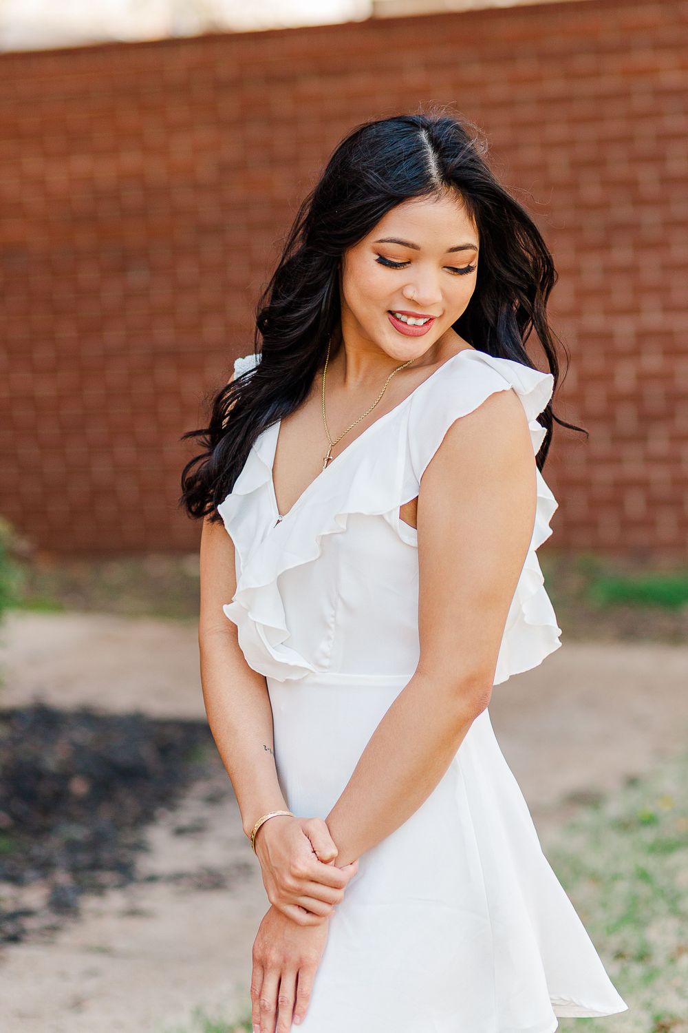 A graduate in a white ruffled dress smiles warmly during outdoor portrait session.