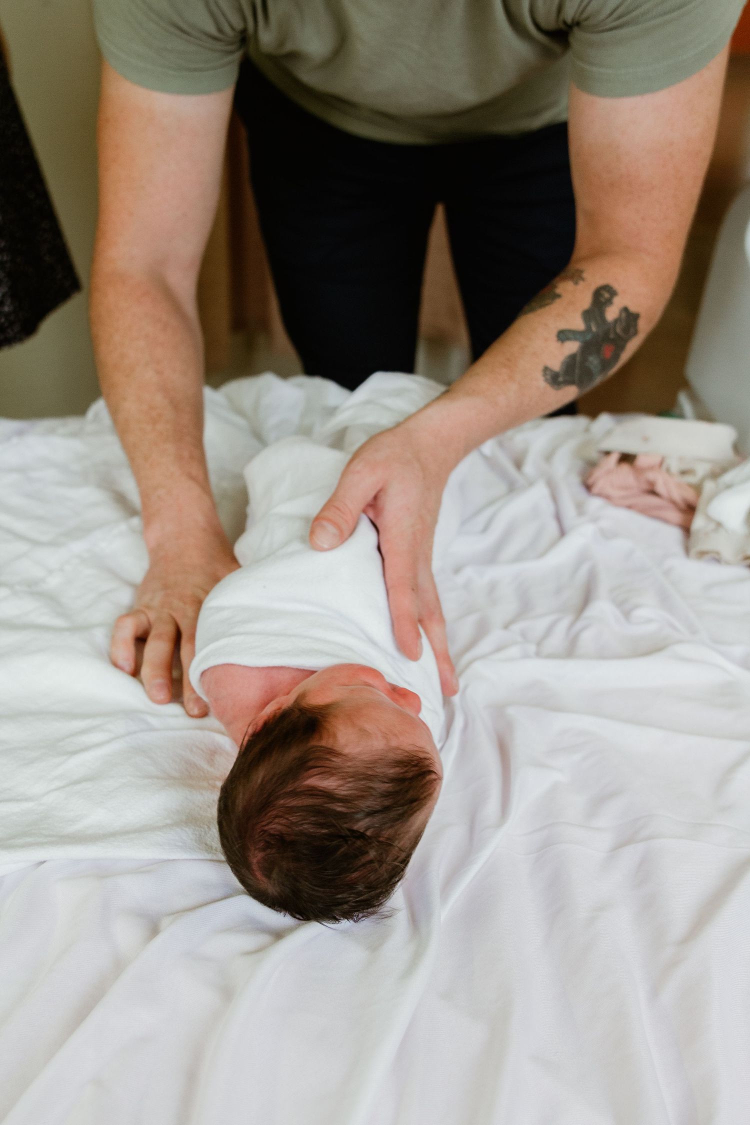A caregiver in a green shirt tends to a newborn on white bedding.