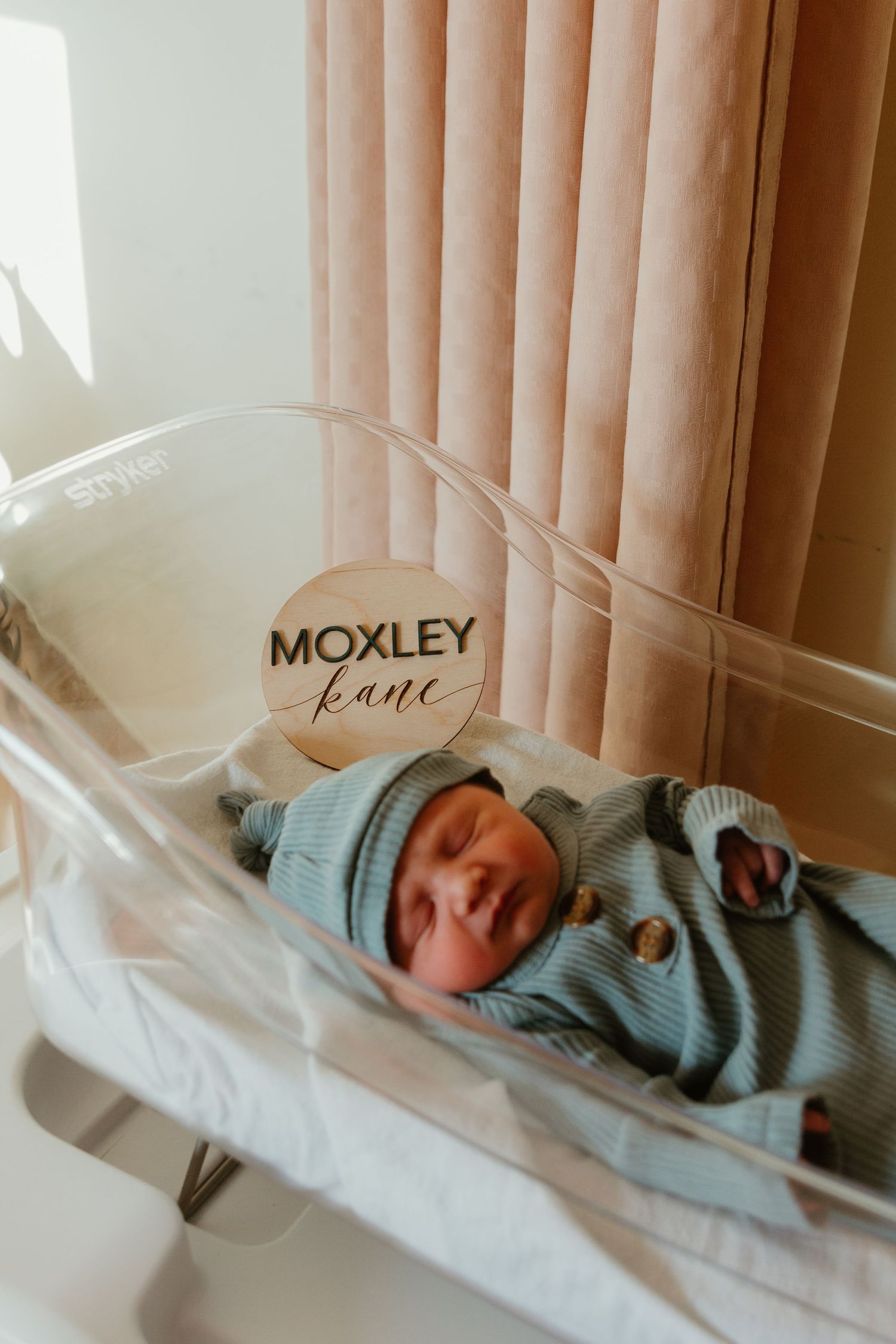 Newborn baby sleeping peacefully in blue outfit with Moxley name sign visible.