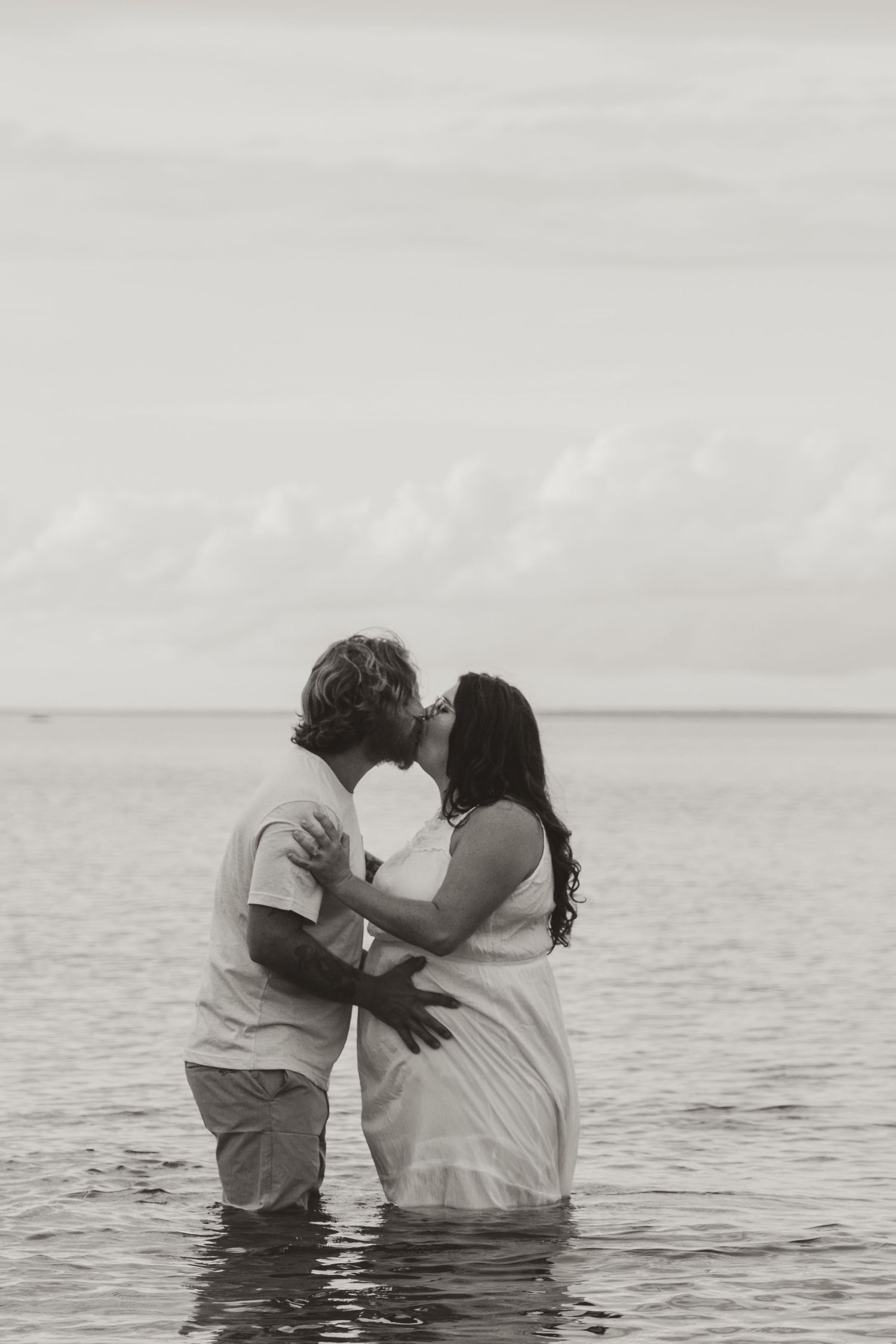 A romantic couple shares a tender moment while standing in ocean waters at sunset.