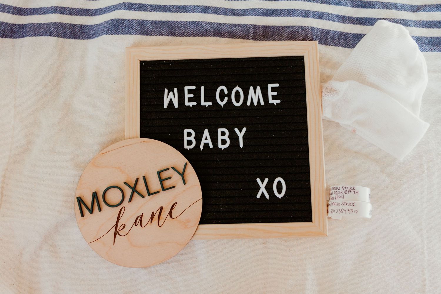 Welcome baby announcement sign with wooden Moxley Kane name plaque on white fabric.