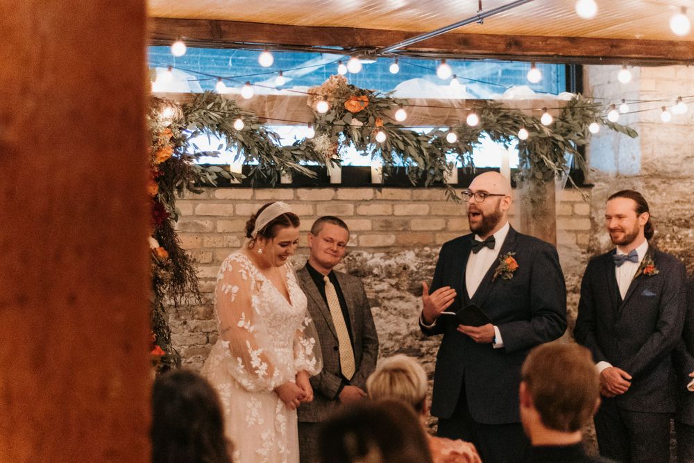 Couple shares a joyful moment during indoor wedding ceremony with string lights.