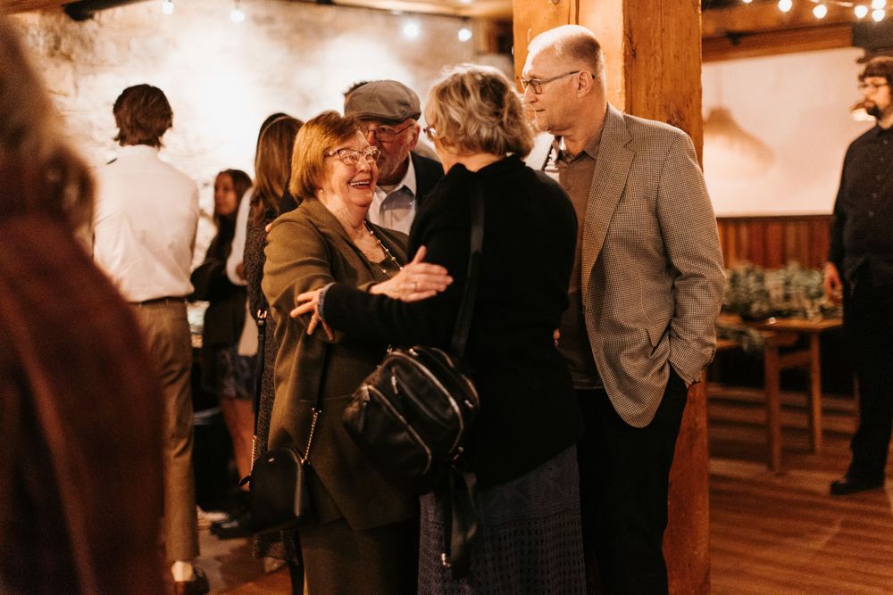 Guests mingling and embracing at a warmly lit indoor wedding reception venue.