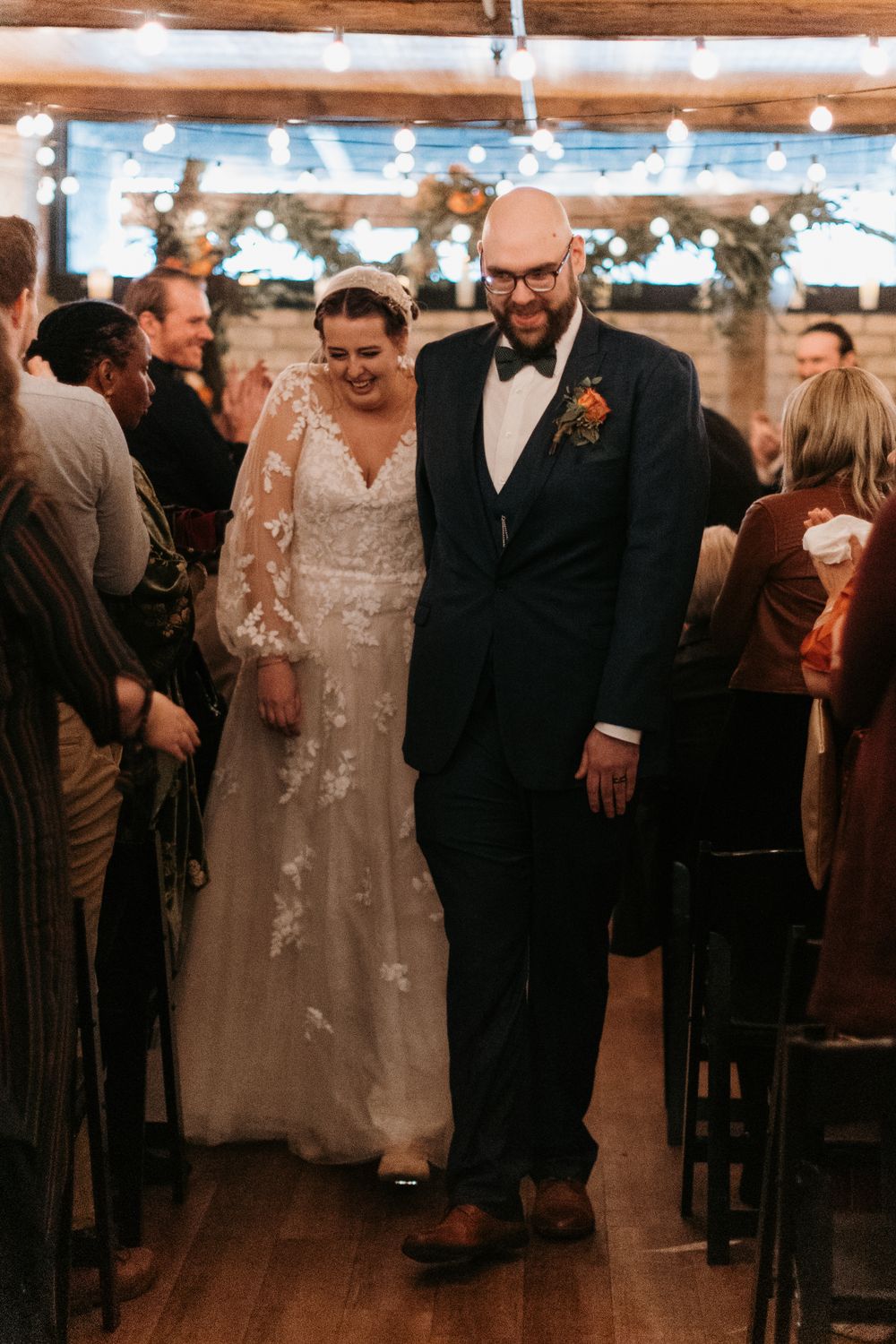 Happy bride and groom smile while walking down the aisle in a warmly lit rustic stone venue.
