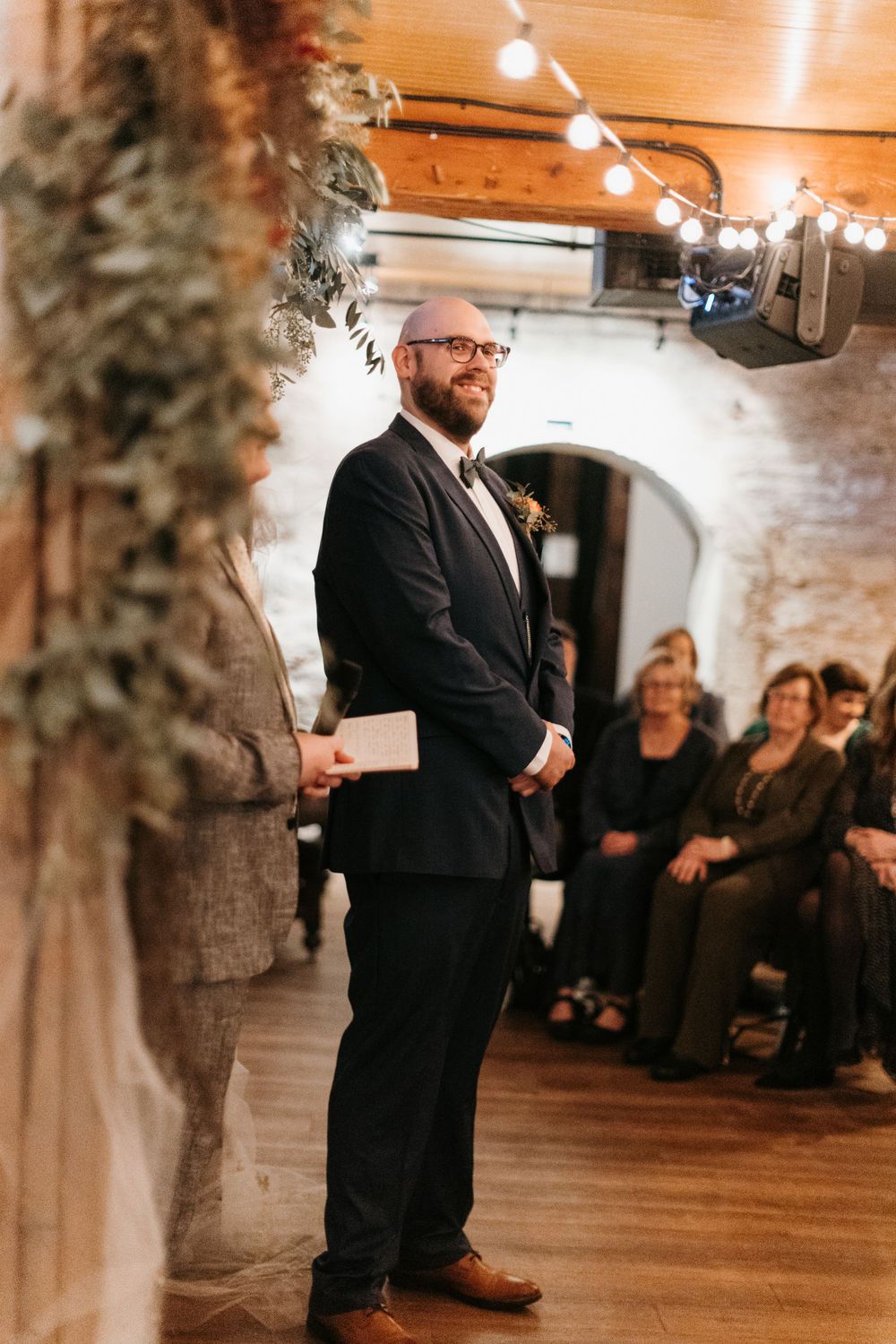 Smiling bearded groom in navy suit awaits his bride at the wedding altar.