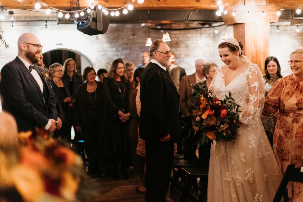 Bride smiles joyfully as she reaches the altar holding a colorful fall bouquet.