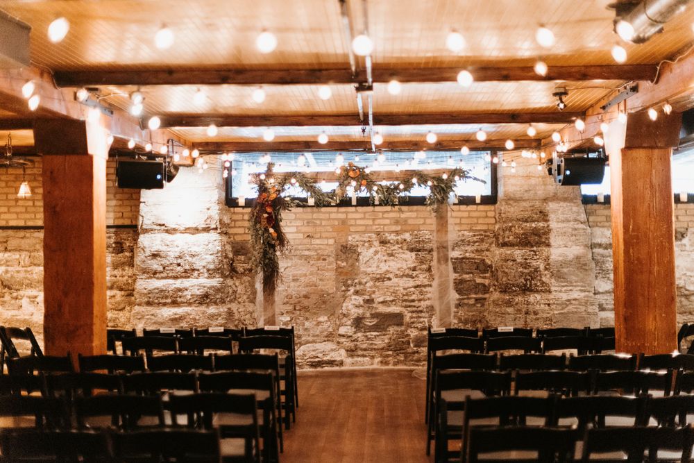 Rustic wedding ceremony venue with string lights, brick walls, and rows of chairs.