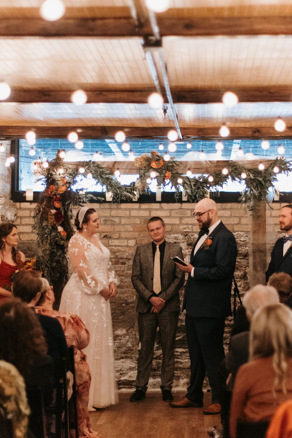 Groom reads vows to bride at rustic indoor ceremony with exposed brick walls.
