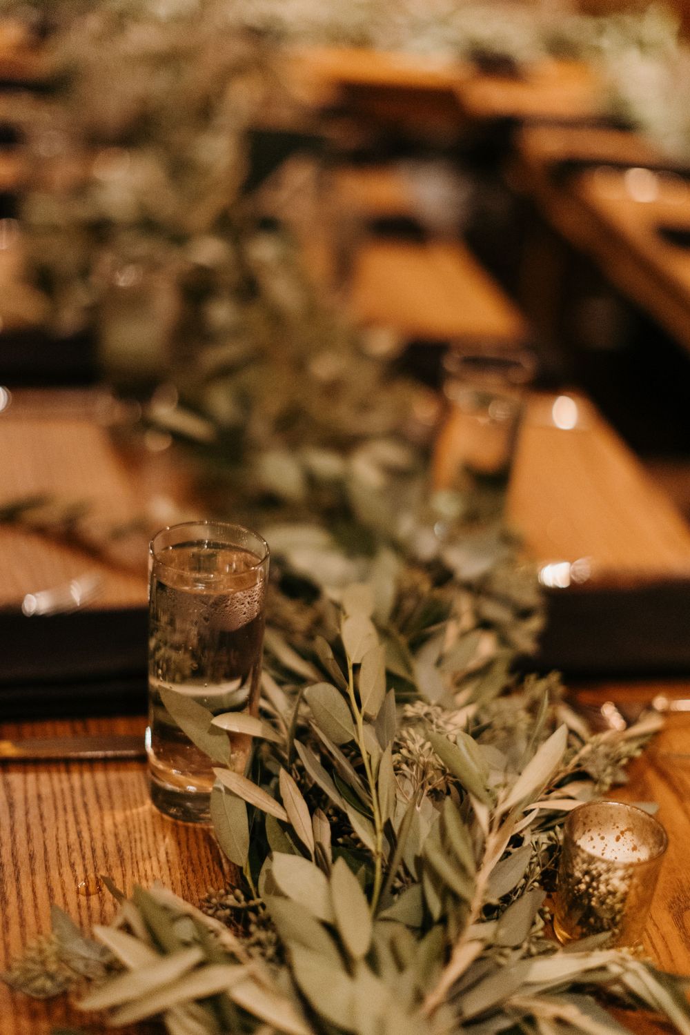 Greenery table runner with candles on wooden reception tables at a wedding.