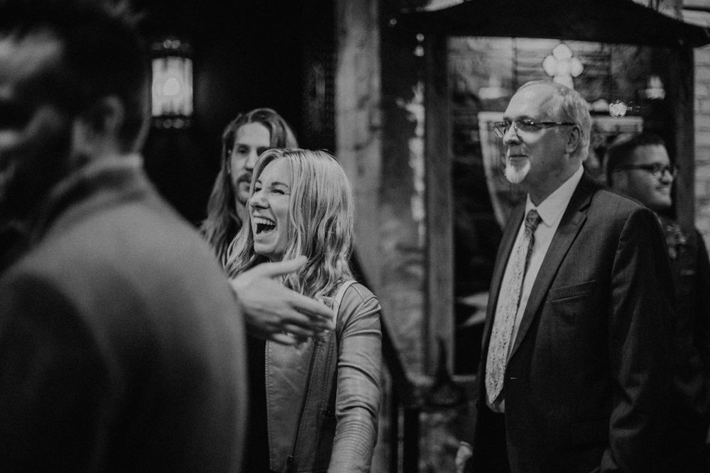 Black and white photo of wedding guests laughing and socializing at a venue.
