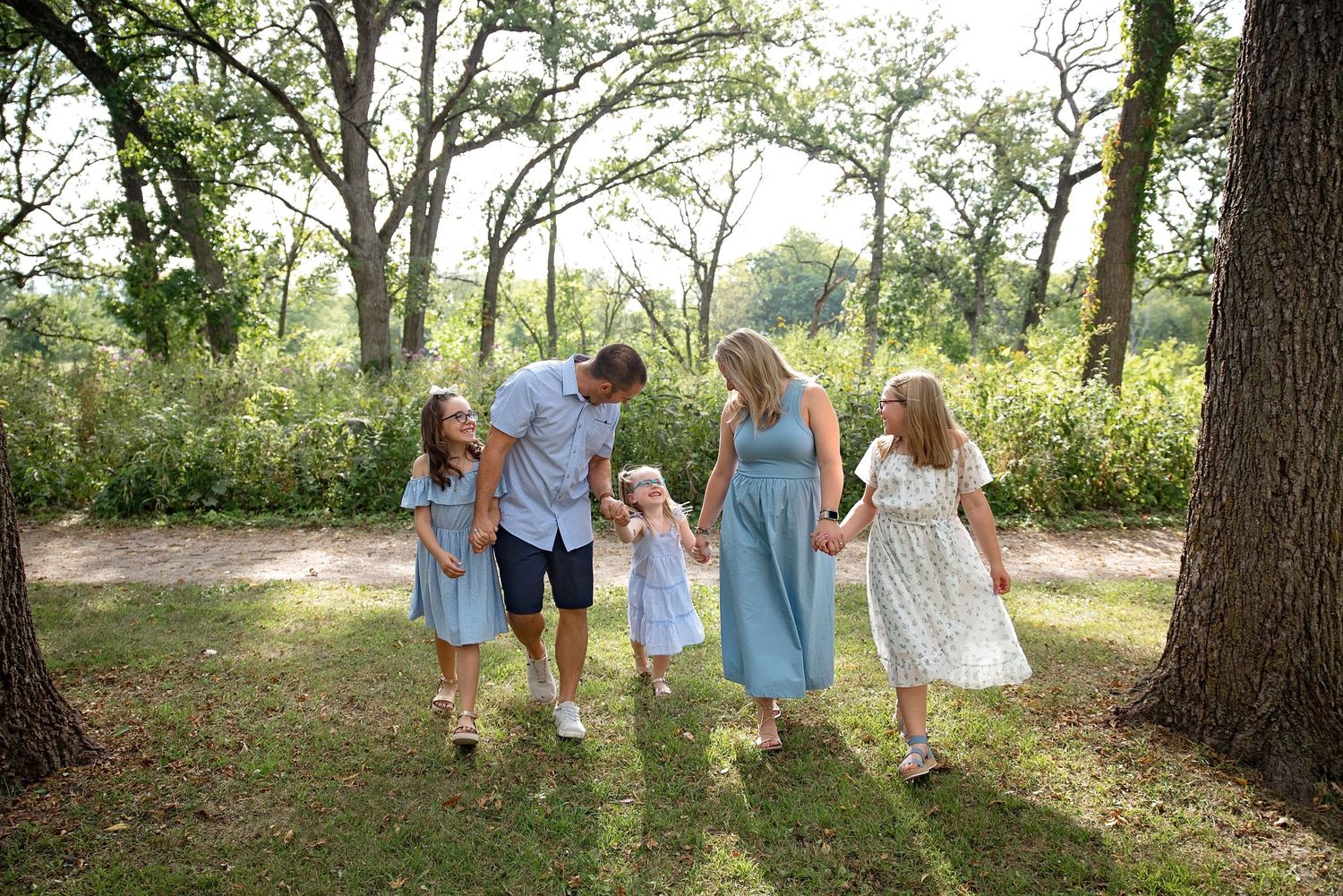 Happy family of five walking hand in hand through a sunny green wooded park.