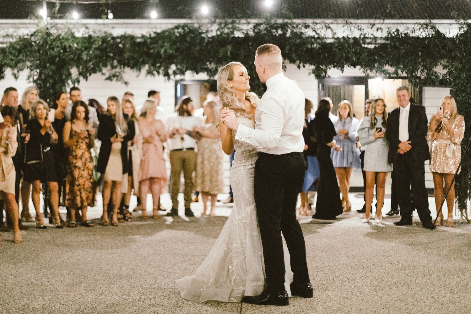 Outdoor wedding reception with string lights and guests gathered for dancing.