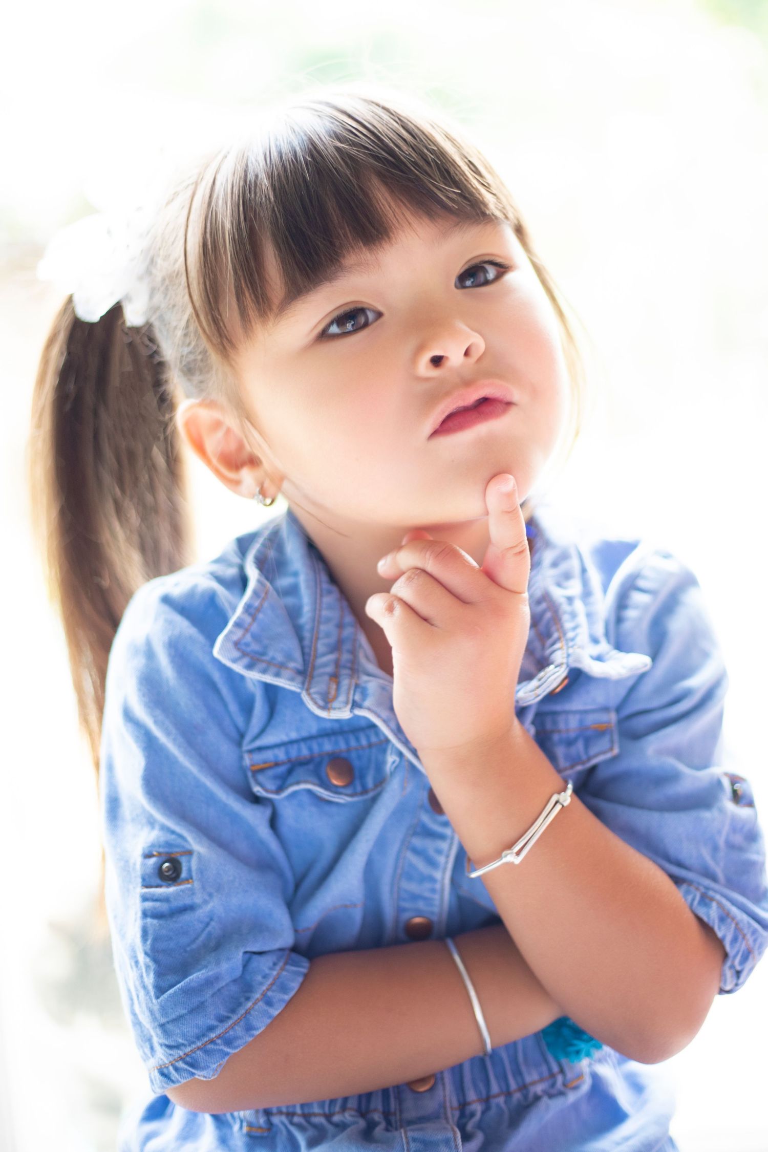 Child in denim jacket posing playfully against bright white background.