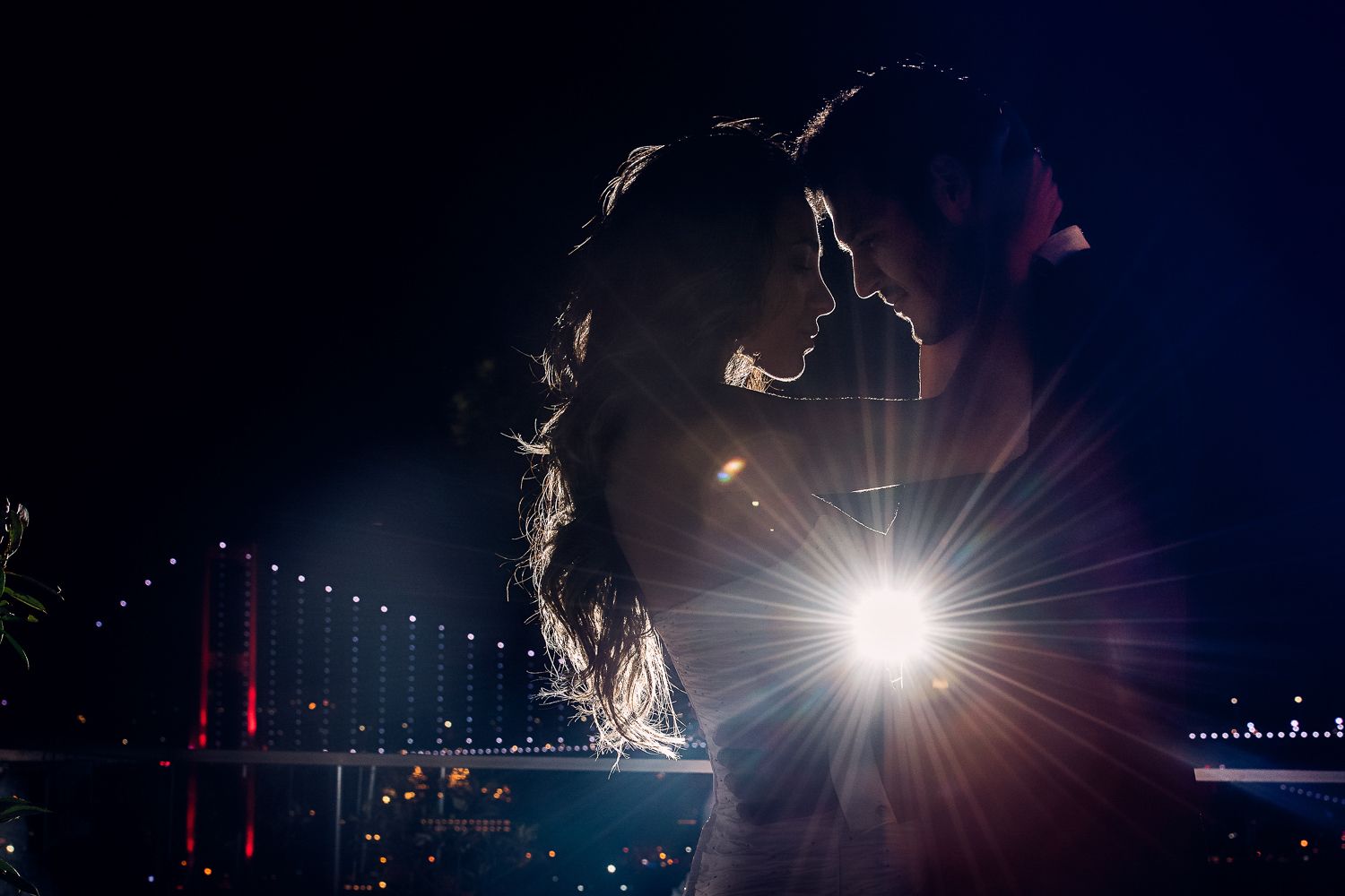 Silhouetted couple against night sky with bridge and lens flare in background.