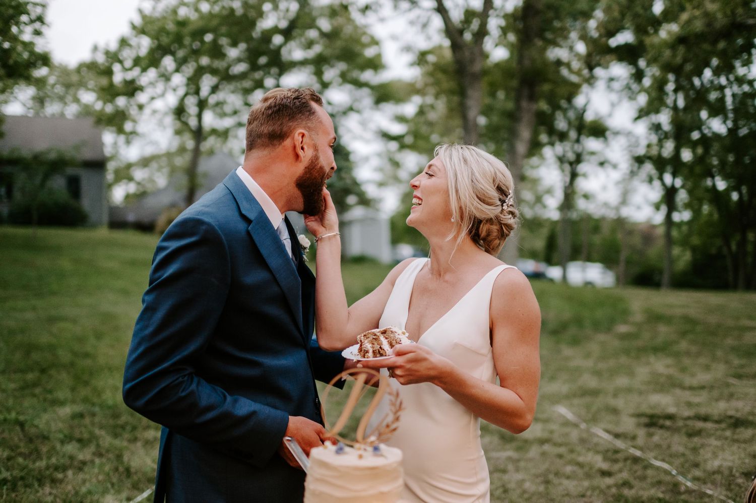 Wedding couple feeding each other cake during their outdoor reception celebration.