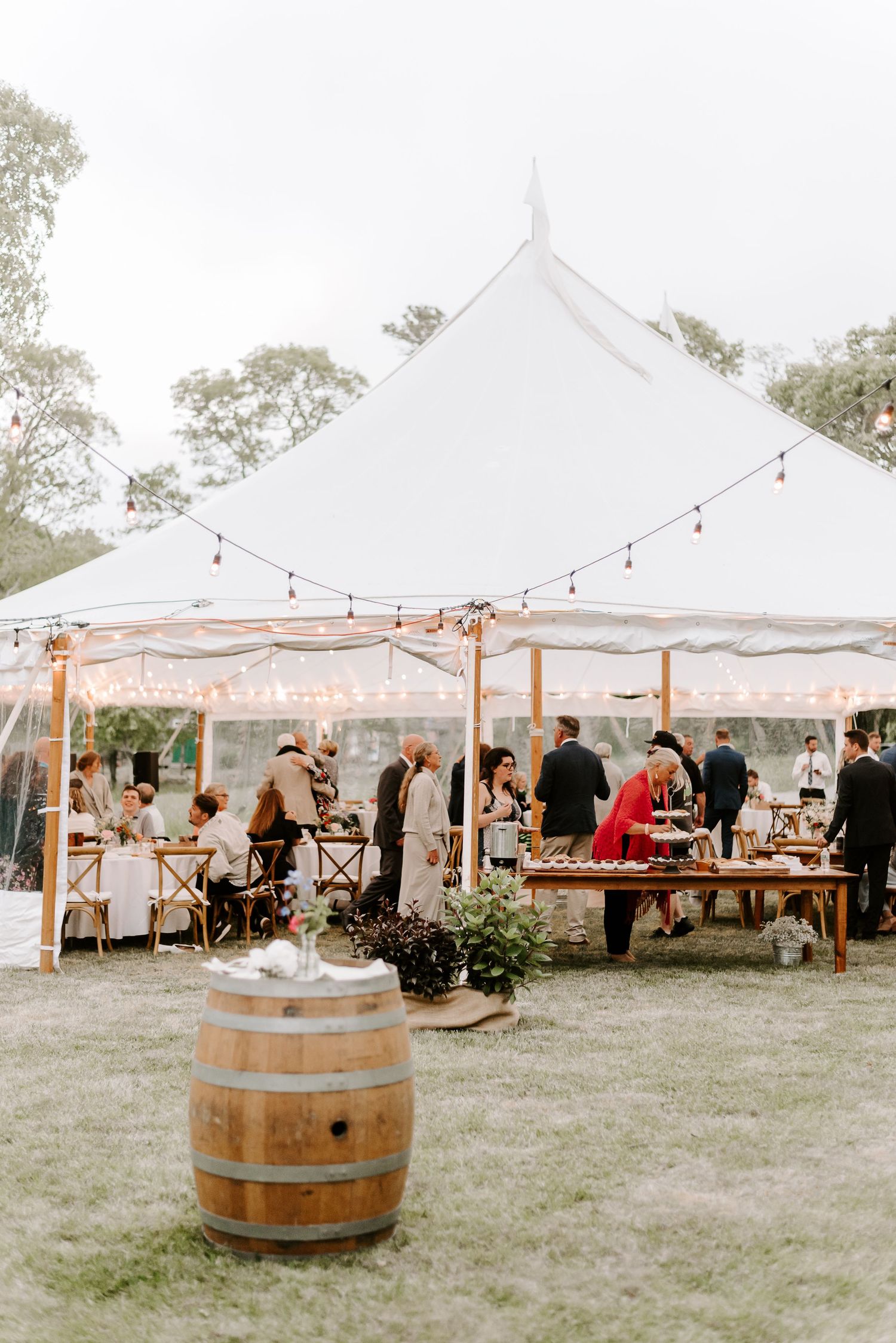 White wedding tent setup in a grassy field with wine barrels and string lights creating an elegant atmosphere.
