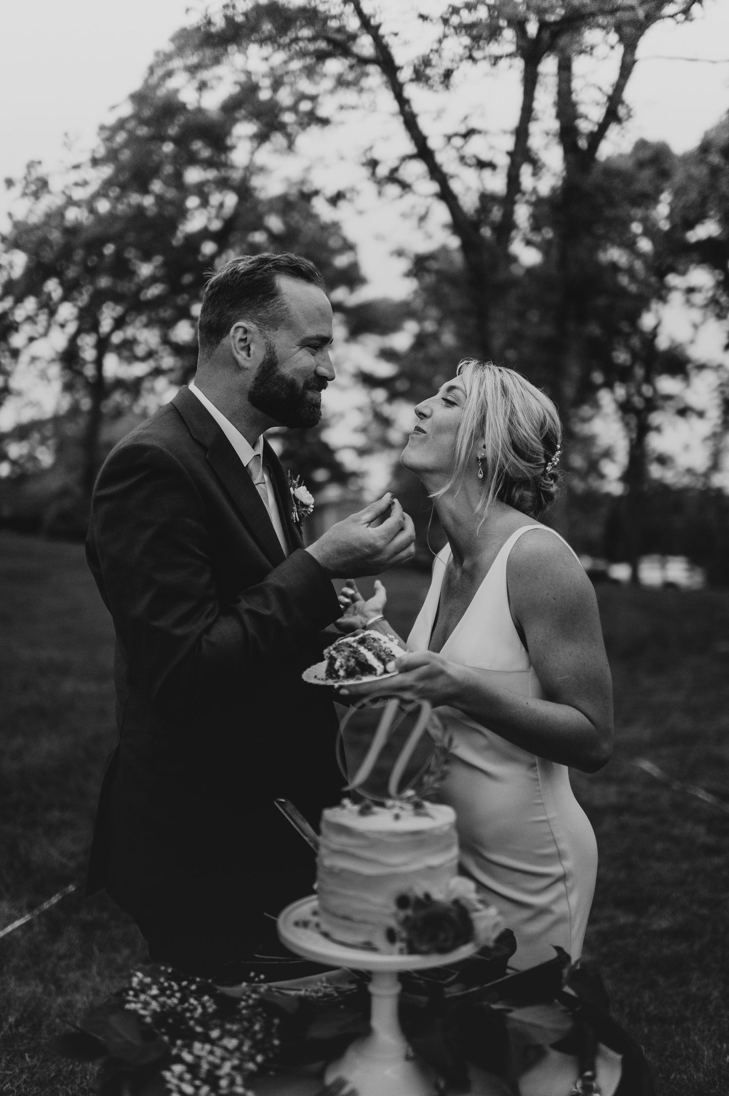 Couple shares playful moments while enjoying wedding cake at their outdoor celebration.