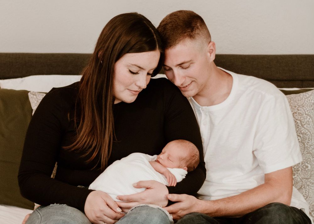 Family sharing quiet moment together on brown couch with newborn.
