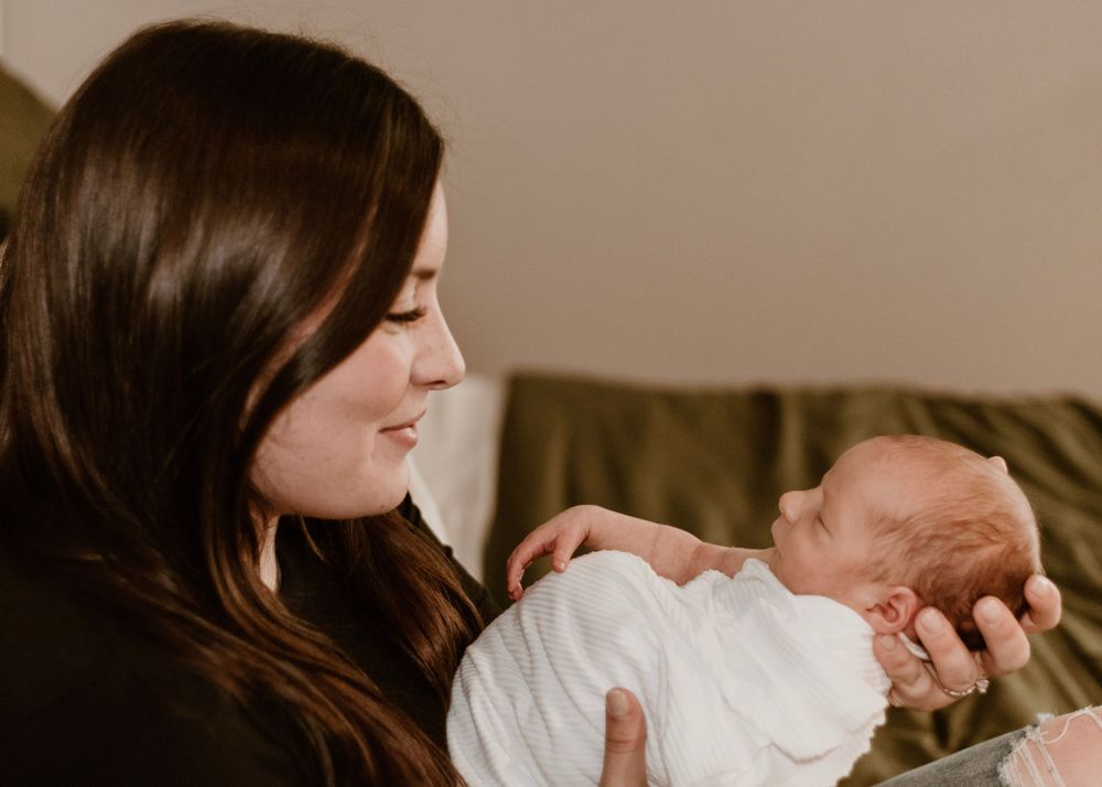 Parent holding sleeping newborn in black sweater against neutral background.