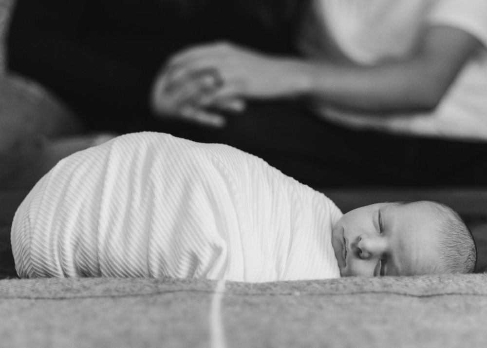 Newborn wrapped in white swaddle lying on grey carpet in black and white photo.