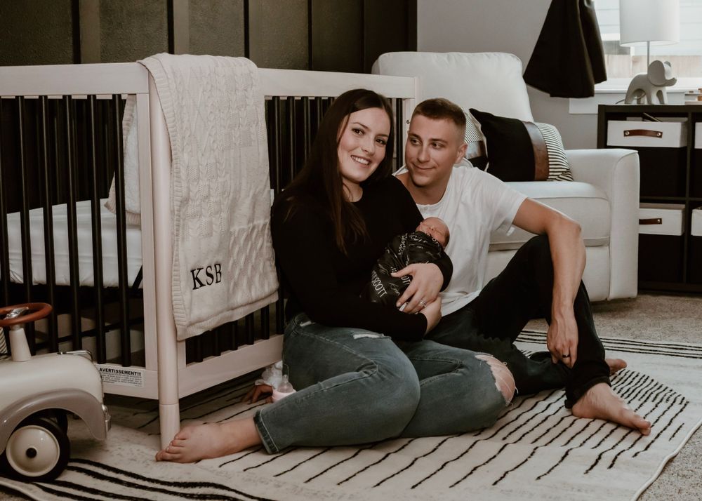 Couple sitting casually on floor near nursery crib in modern room setting.