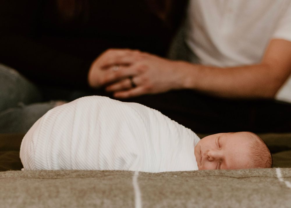 Newborn baby wrapped in white cloth lying peacefully on a plush carpet.